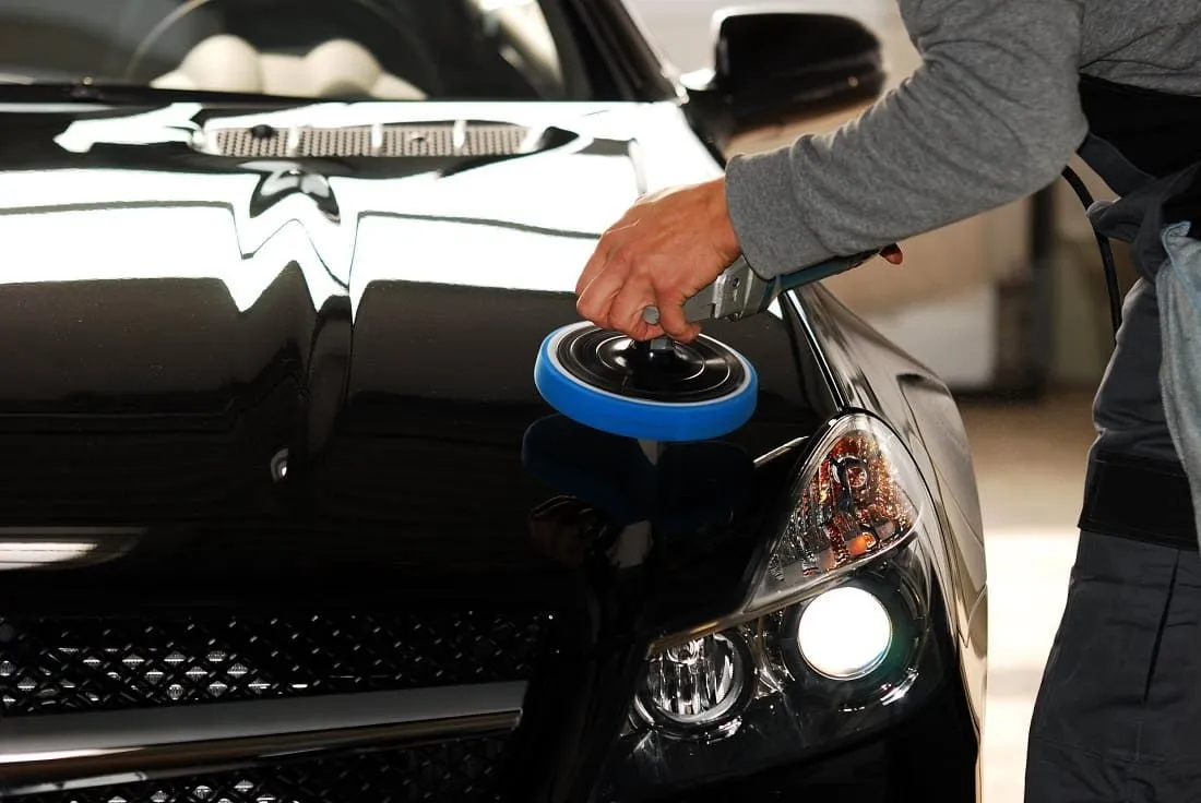 Technician machine polishing the paint on a black car