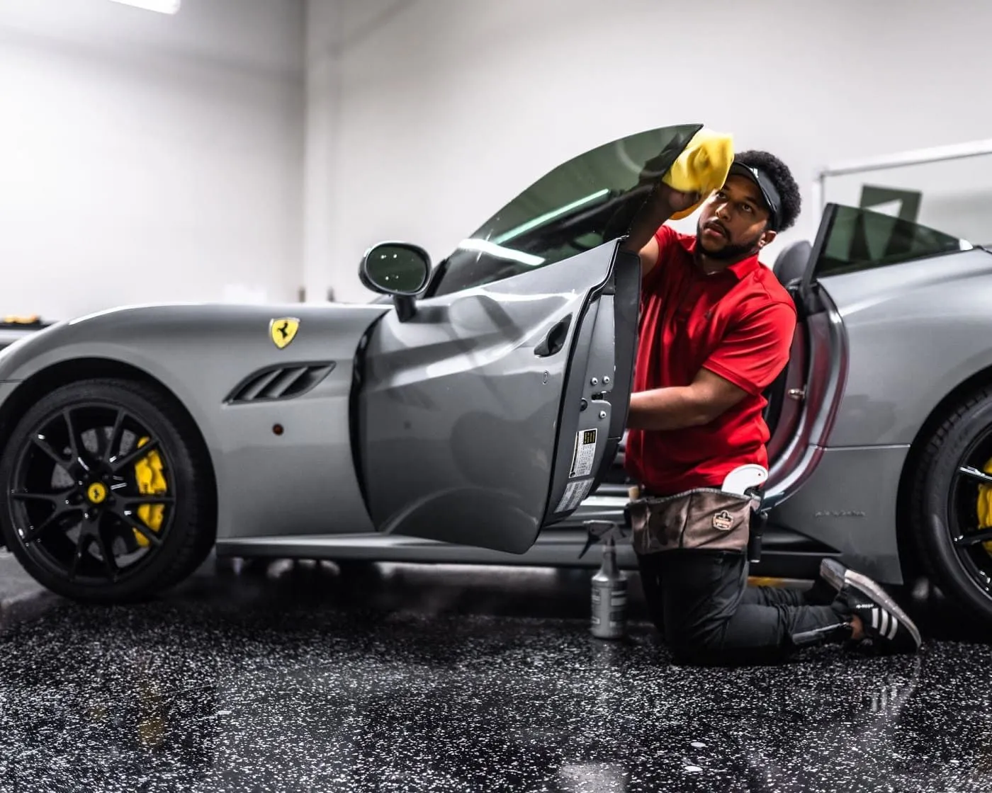 Technician applying film to a gray Ferrari inside the shop