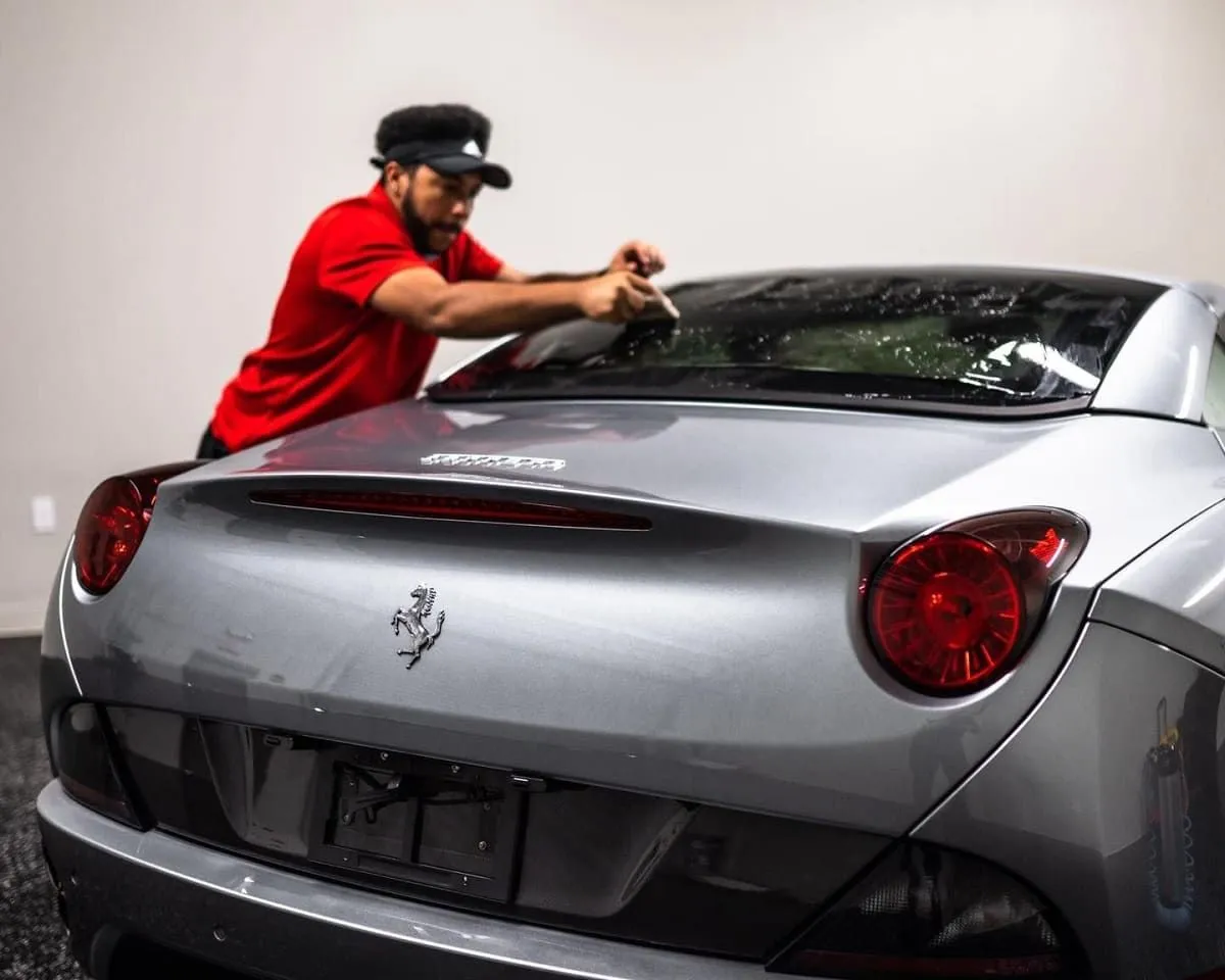 Technician applying film to the rear glass of a gray Ferrari