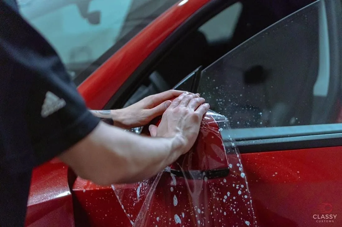 Installer squeegeeing paint protection film onto a red car door