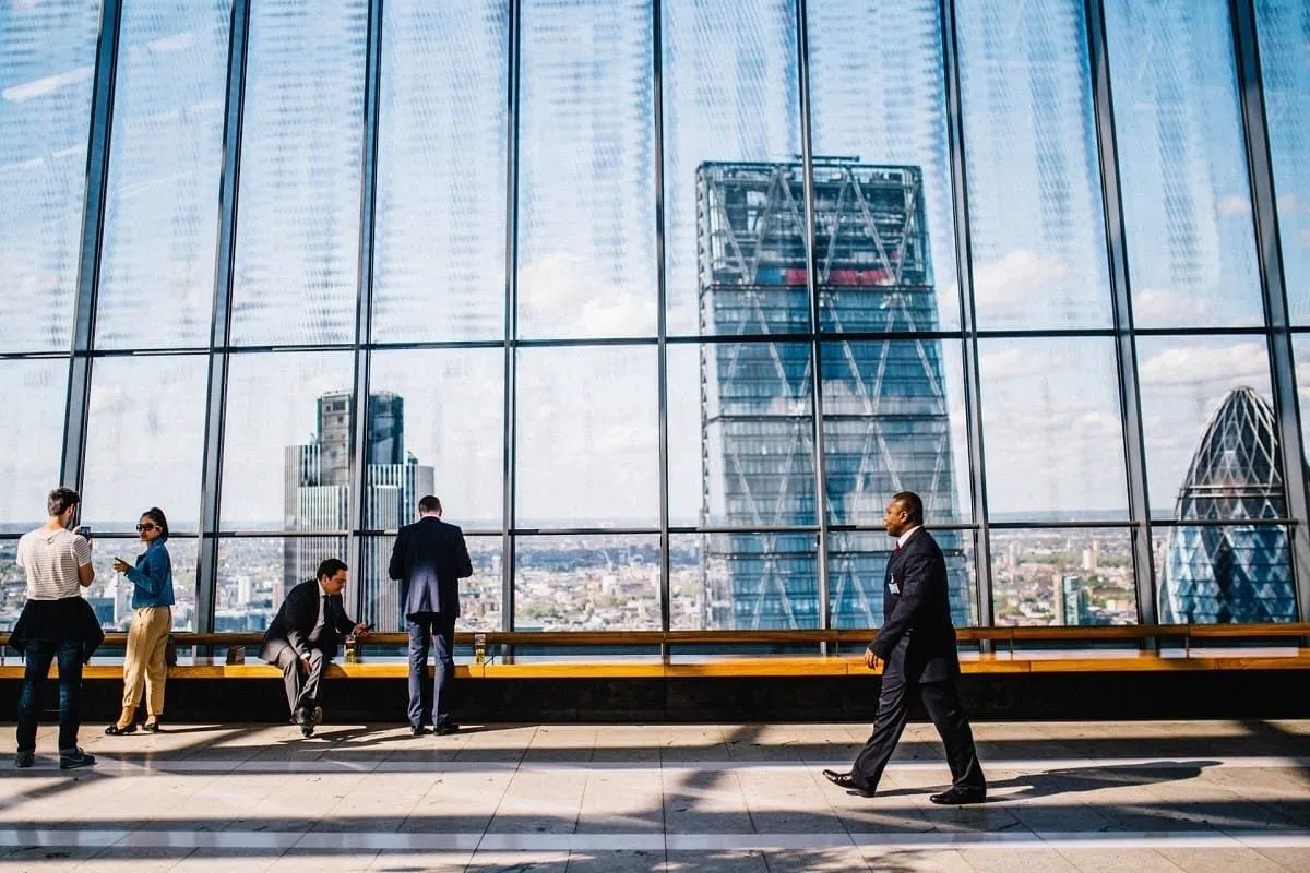People walking along a glass wall overlooking a city